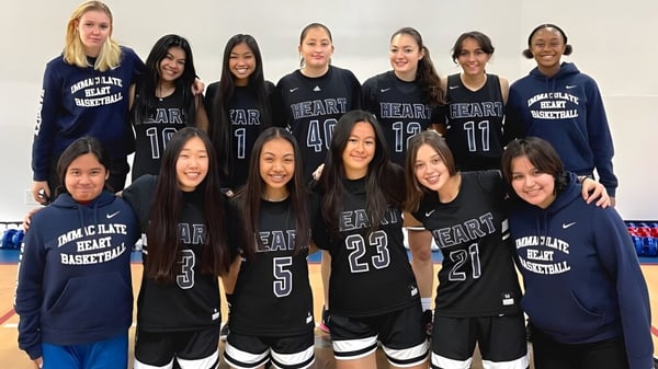 Un grupo de estudiantes de la Immaculate Heart Central School posan en uniformes de baloncesto frente a un fondo blanco.