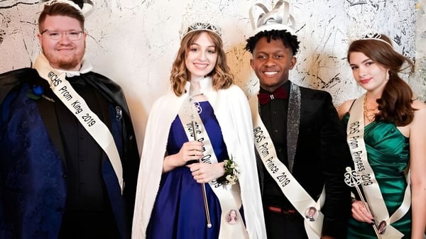 Cuatro personas vestidas formalmente posan frente a una pared cubierta de graffiti en el campus de la Indian River Charter High School.