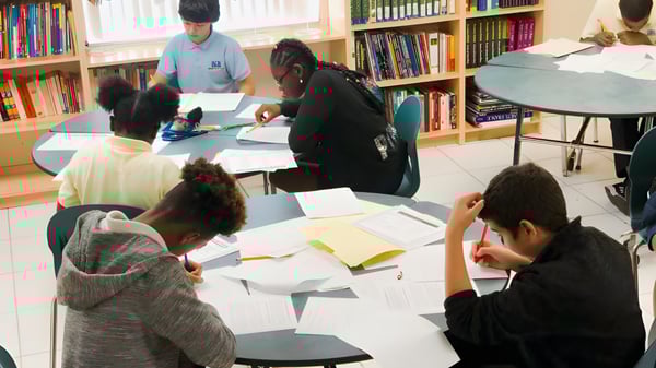 Un grupo de estudiantes de la International School of Broward estudia junto en la biblioteca rodeados de estanterías de libros.