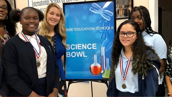 Estudiantes de la International School of Broward están con medallas frente al banner de un concurso de Science Bowl.