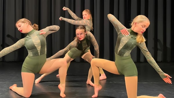 Estudiantes de Ipswich High School realizan una presentación de danza sincronizada en un escenario con fondo negro.