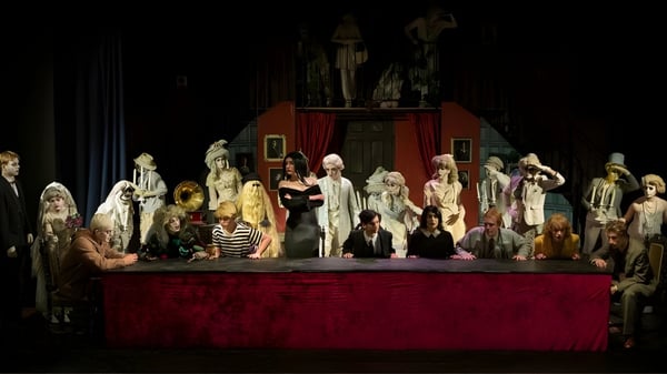 Un grupo de personas en trajes está en el escenario de la Ipswich School frente a un telón rojo con un fondo decorativo.