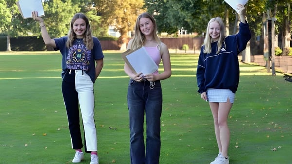 Tres estudiantes de la Ipswich School están en un parque sobre una pradera y sonríen a la cámara.