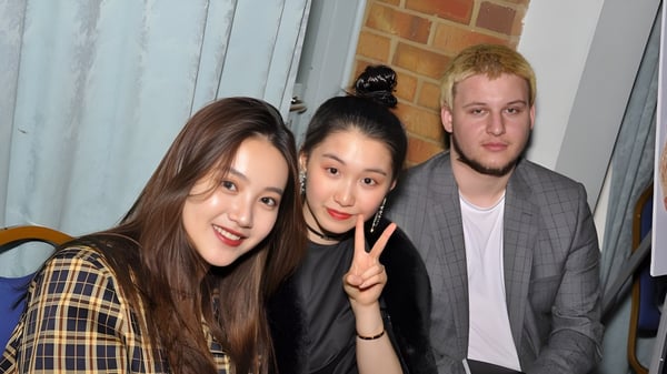 Tres estudiantes de la International School of Creative Arts posan juntos frente a una pared de ladrillo en el área de residencia.