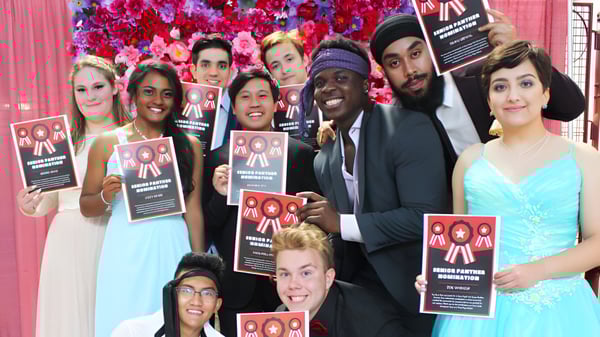 Estudiantes de la J. Percy Page High School sostienen carteles por la reforma de inmigración frente a un colorido fondo de flores.