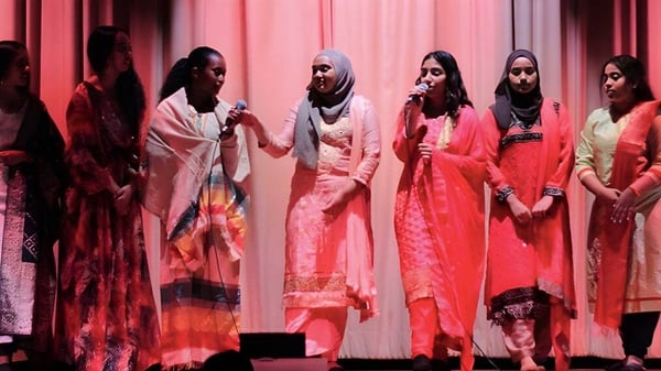 Un grupo de estudiantes en coloridos trajes tradicionales está en el escenario del Jarvis Collegiate Institute.
