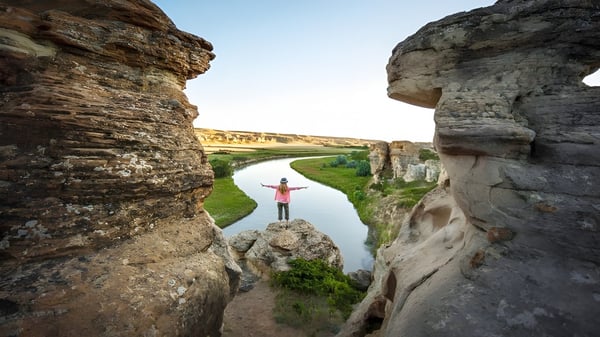 Una persona está de pie sobre una roca y mira hacia un río en un paisaje impresionante en el campus de Jasper Place High School.