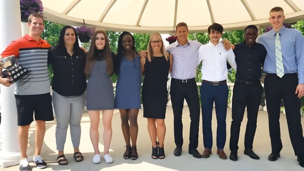 Un grupo de estudiantes está de pie en círculo frente a un fondo verde en el campus de Jasper Place High School.