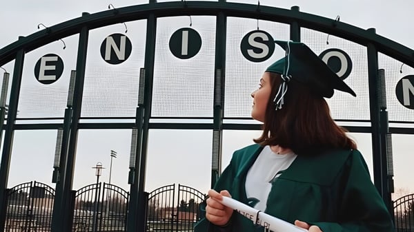 Una persona con abrigo verde está frente a la gran puerta de metal con la inscripción ENOSC en el terreno de la Jenison High School.