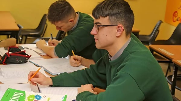 Dos estudiantes en uniformes verdes están sentados concentrados en el aula de la Jesus and Mary Secondary School y trabajan en tareas.