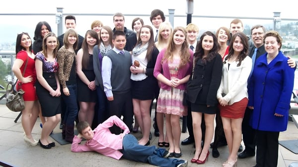 Un grupo de estudiantes de la John Maland High School está de pie al aire libre frente a un paisaje urbano.