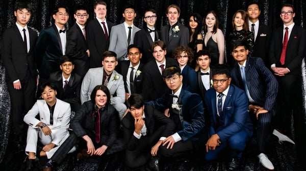 Un gran grupo de estudiantes vestidos formalmente posan para una foto grupal en el John Paul College.