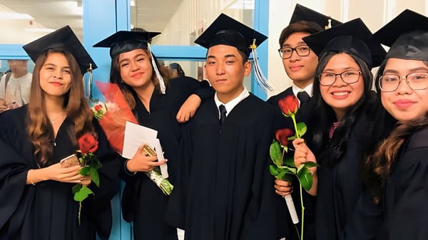 Un grupo de graduados en vestimenta de graduación posan con flores en el campus del John Polanyi Collegiate Institute.