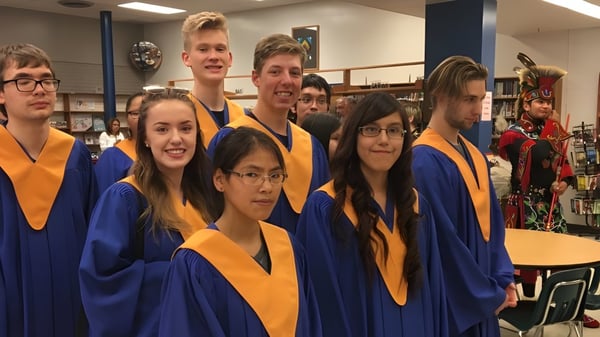 Un grupo de estudiantes del John Taylor Collegiate posan en sus togas de graduación en un aula.