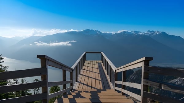 Un camino de madera conduce hacia una cadena montañosa bajo un cielo azul en el terreno de la Johnston Heights Secondary School.