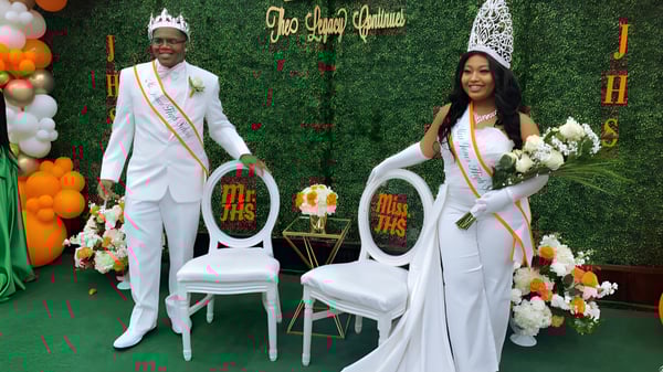 Un hombre y una mujer en ropa formal están en un evento en el campus de la Jones High School frente a un fondo decorativo con flores y globos.