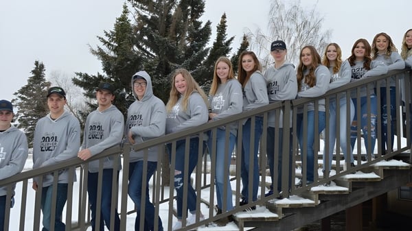 Estudiantes de la J.T. Foster High School están en un balcón de madera con árboles nevados de fondo.