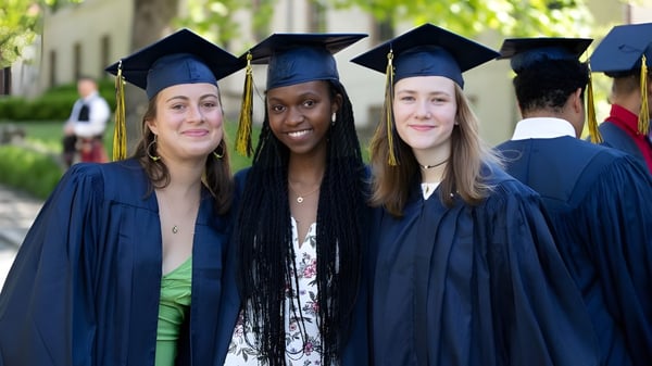 Tres estudiantes en ropa de graduación están juntos en el campus de la J.T. Foster High School frente a árboles y edificios.