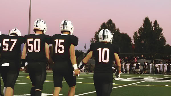 Un grupo de jugadores de fútbol americano de la Justin Siena High School está en el campo al atardecer.