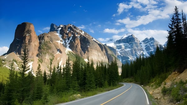 Una carretera sinuosa atraviesa un paisaje boscoso con montañas nevadas al fondo cerca de la J.V. Humphries Secondary School.