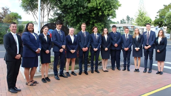 Un grupo de estudiantes de Kaipara College está en un área exterior pavimentada rodeada de árboles.