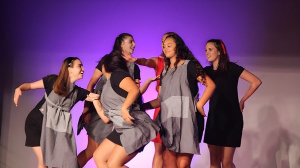 Cuatro estudiantes del Kapiti College están juntas en un escenario frente a un fondo violeta.