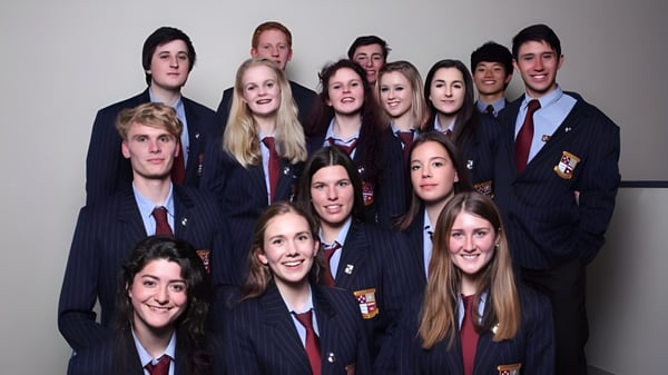 Un grupo de estudiantes del Kapiti College posan juntos en uniforme escolar frente a un fondo de un solo color.