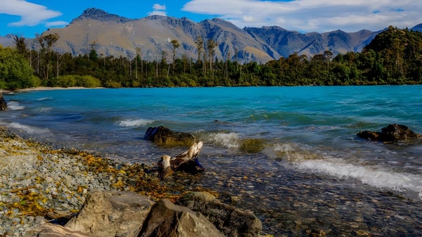 Un tranquilo lago alpino con montañas nevadas y una orilla rocosa cerca del Kapiti College.