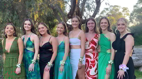 Un grupo de jóvenes mujeres en vestidos coloridos se agrupan en el terreno de la Kapunda High School frente a árboles.