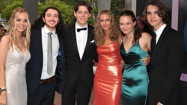 Un grupo de estudiantes bien vestidos posan sobre una alfombra roja en el evento del Kawana Waters State College.