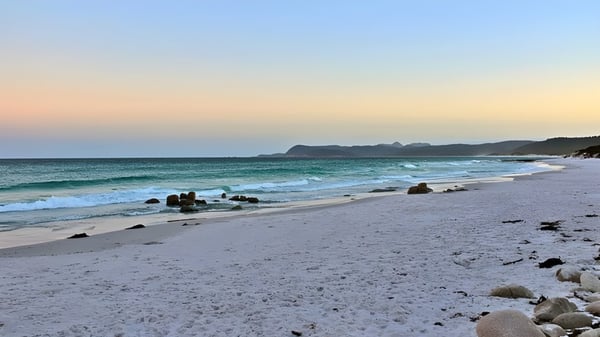 Una playa tranquila con olas y rocas bajo el cielo al atardecer en los alrededores del Kawana Waters State College.