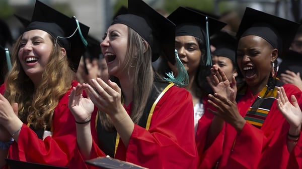 Un grupo de graduados en togas rojas y birretes celebra su graduación en la Keebra Park State High School.