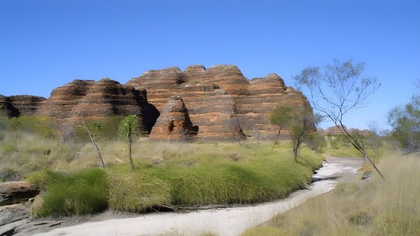 Un camino de tierra sinuoso atraviesa un prado hacia rocas de arenisca bajo un cielo azul en el terreno de la Kelmscott Senior High School.