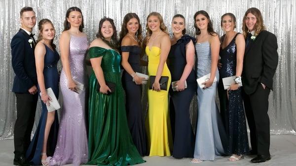 Un grupo de personas elegantemente vestidas posan frente a un fondo plateado en el campus de la Kelmscott Senior High School.