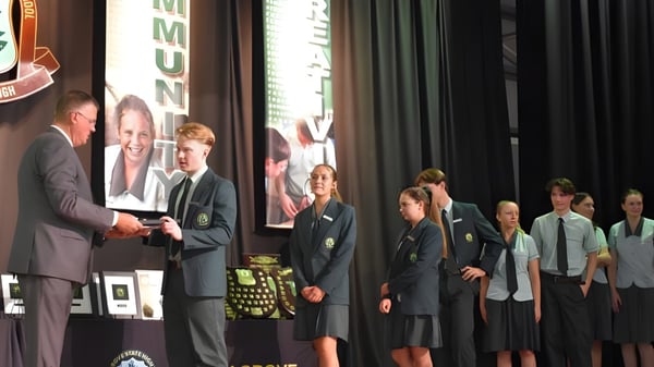 Estudiantes del Kelvin Grove State College reciben un premio en el escenario de un hombre en traje.