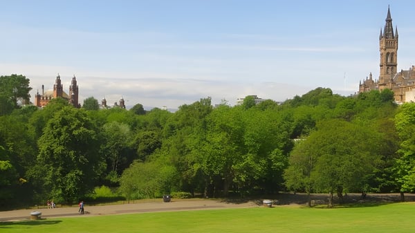 Personas pasean por un parque verde con árboles y una catedral histórica al fondo en el Kelvin Grove State College.
