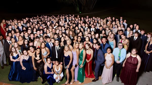 Un grupo de personas en ropa formal en una celebración con fuegos artificiales de fondo en el campus de la Kenmore State High School.