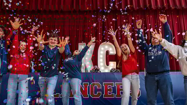 Un grupo de estudiantes de la Kennedy Catholic High School celebra frente a un gran cartel de NCEF con cortinas rojas de fondo.