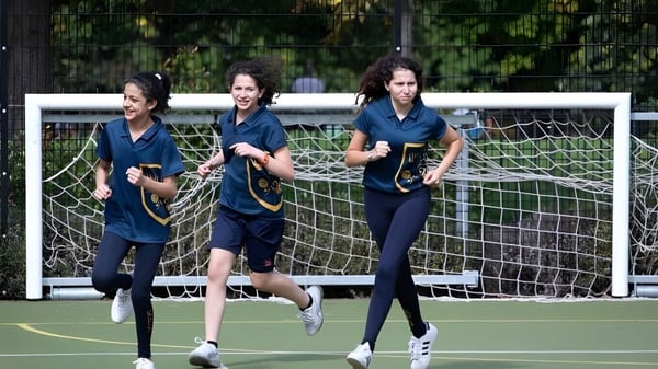 Tres alumnas de Kensington Park School corren en el campo de deportes frente a un poste de gol.