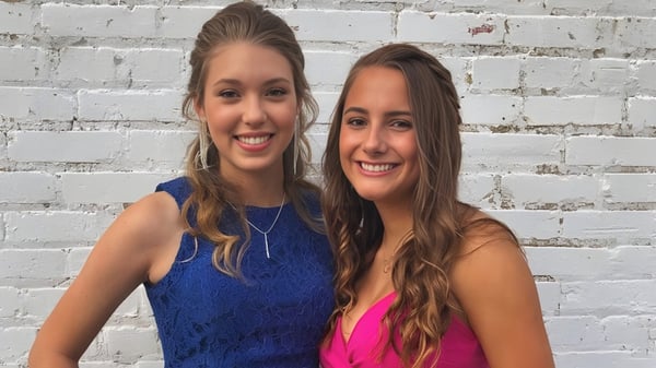 Dos estudiantes de la Kenston Forest School posan sonriendo frente a una pared de ladrillos blancos.
