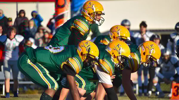 Un grupo de futbolistas en camisetas verdes y amarillas está en el campo de la Kenston Forest School con espectadores al fondo.