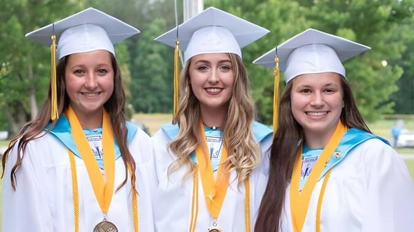 Tres estudiantes de la Kenston Forest School están sonriendo en sus togas de graduación frente a un fondo verde.