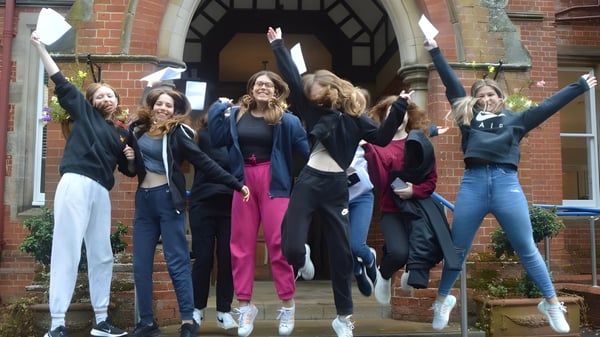 Un grupo de alumnas del Kent College Pembury sale jubilosamente de un edificio de ladrillo.