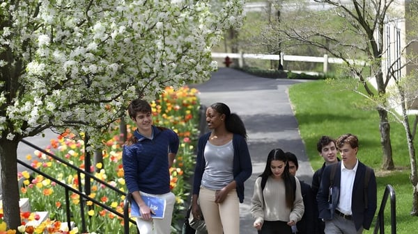 Un grupo de estudiantes de la Kent School camina por un camino flanqueado de árboles en flor y flores de colores.
