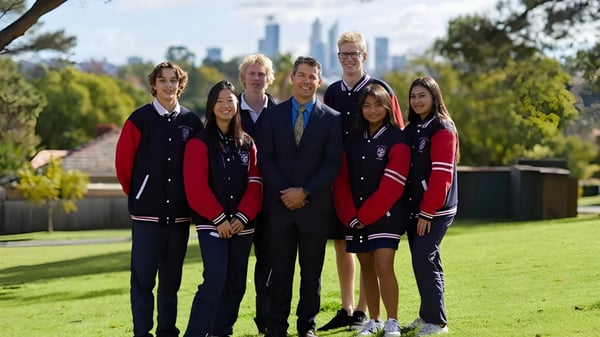 Un grupo de estudiantes de la Kent Street Senior High School posa frente al paisaje urbano con altos edificios.
