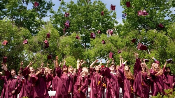 Un gran grupo de graduados de la Kents Hill School celebra bajo árboles verdes sus logros académicos.