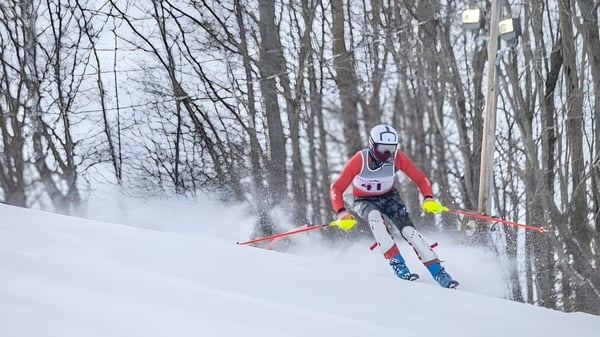 Un esquiador con chaqueta roja baja por una pendiente nevada en el terreno de la Kents Hill School.