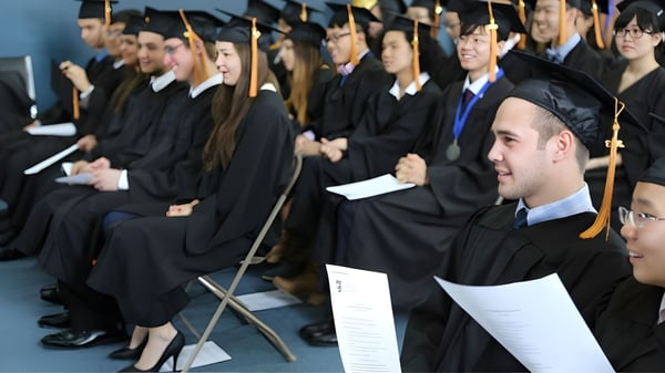 Las graduadas y graduados de la Keystone School están sentados en filas con sus togas de graduación y miran a la cámara.