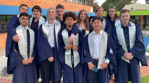 Un grupo de alumnas y alumnos del Kiara College está en sus togas de graduación frente a un edificio de ladrillo.