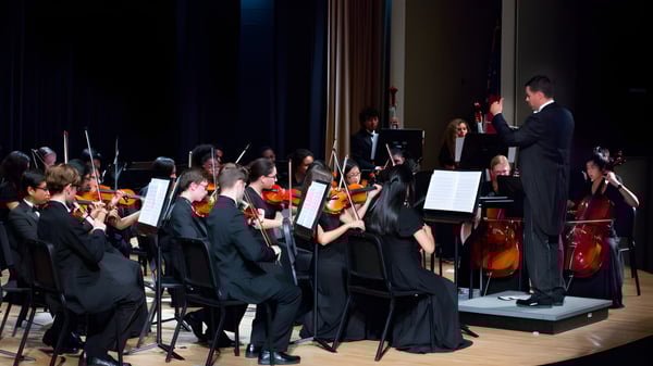 La orquesta sinfónica de la Kilkenny City Vocational School presenta un concierto con músicos y un director en el escenario.